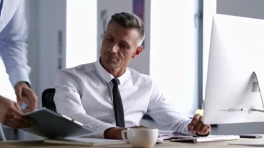 Yakışıklı gülümseyen ofis çalışanı bilgisayar kullanarak ve ofiste meslektaşı ile belgeler hakkında konuşurken