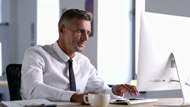 オフィスで働きながら コンピュータを使って白いシャツを着てノートに書き込む真面目な男 — ストック動画