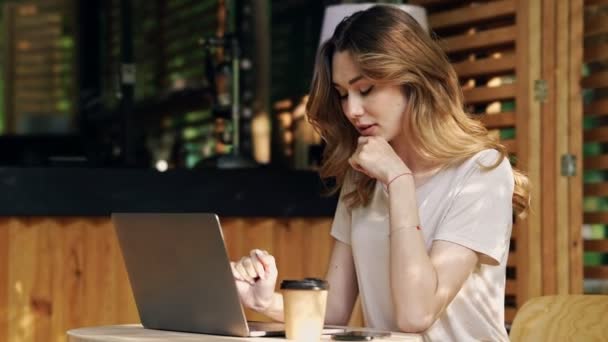 微笑的黑发女人穿着休闲的衣服坐在桌子旁 同时使用笔记本电脑 在户外咖啡馆喝咖啡 — 图库视频影像