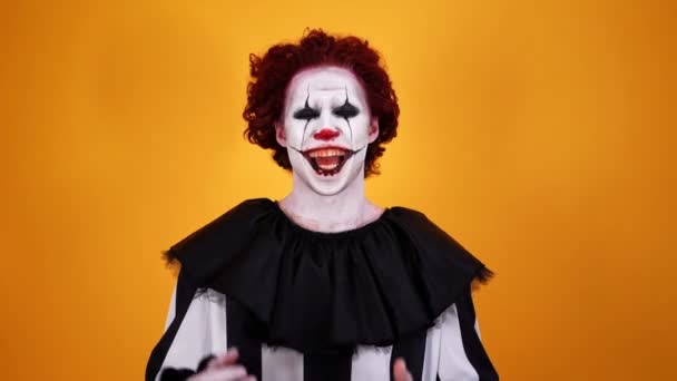 笑神秘的小丑与万圣节化妆看着相机在橙色背景 — 图库视频影像