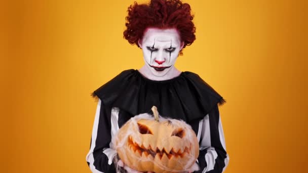 Angry Clown Halloween Makeup Holding Pumpkin Looking Camera Orange Background — Stock Video
