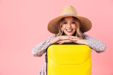 Mutlu genç güzel kadın turist bavul ile pembe duvar arka plan üzerinde izole poz.