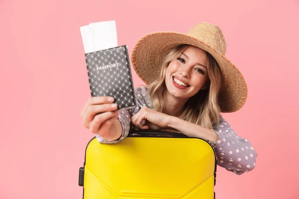 Heyecanlı genç güzel kadın turist biletleri ile pasaport tutan bavul ile pembe duvar arka plan üzerinde izole poz. — Stok fotoğraf