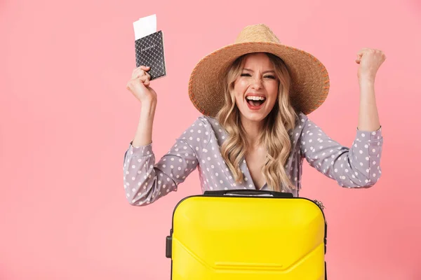 Upphetsad ung vacker kvinna turist poserar isolerade över rosa vägg bakgrund med resväska Holding pass med biljetter. — Stockfoto