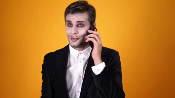 Turuncu Arka Plan Üzerinde Akıllı Telefon Tarafından Konuşurken Cadılar Bayramı — Stok video