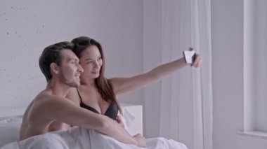 Evde yatakta birlikte yatarken akıllı telefon kullanarak neşeli seven çift