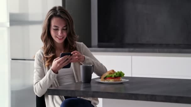 Mulher Morena Feliz Usando Smartphone Enquanto Sentada Mesa Cozinha — Vídeo de Stock