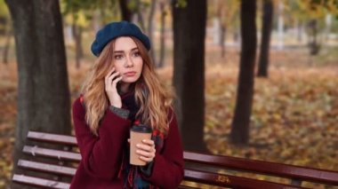 Parkta bankta otururken akıllı telefon ile konuşan bere şapka ve palto sıkılmış esmer kadın