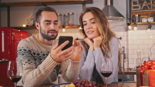 自宅で一緒にロマンチックな夜を過ごしながら ワインを飲み スマートフォンを使用して楽しい素敵なカップル — ストック動画