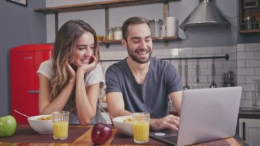 Gülümseyen güzel çift kahvaltı ve mutfakta birlikte otururken dizüstü bilgisayar kullanarak