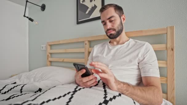 Poważny Brodaty Człowiek Pomocą Smartfona Leżąc Łóżku Sypialni — Wideo stockowe