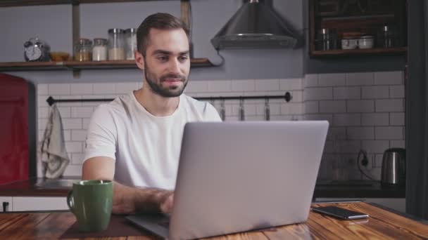 微笑英俊的胡子男子使用笔记本电脑 而坐在桌旁在家里 — 图库视频影像
