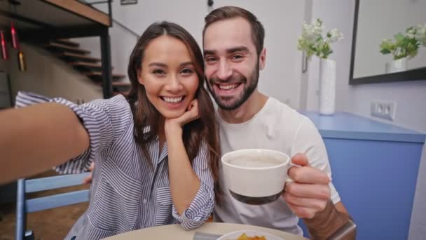幸せな素敵なカップルは 朝食を持って キッチンで一緒に座っている間 自分撮りを作ります — ストック動画