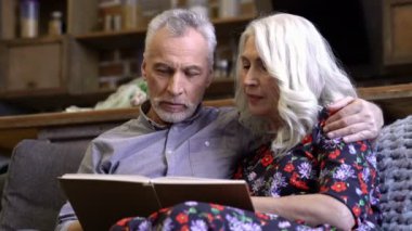 Neşeli yaşlı zarif çift kanepede birlikte oturan ve evde photoalbum bakıyor