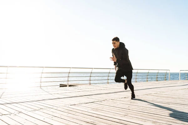 Zdjęcie przystojnego sportowca biegnąc morzem wzdłuż drewnianego dzika — Zdjęcie stockowe