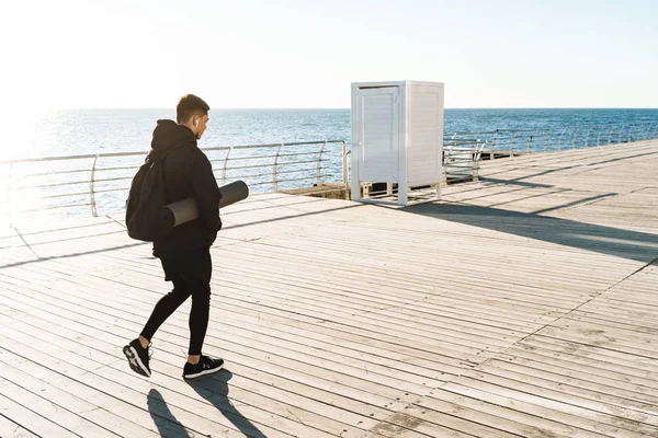 Photo d'un sportif sportif portant des écouteurs marchant au bord de la mer — Photo