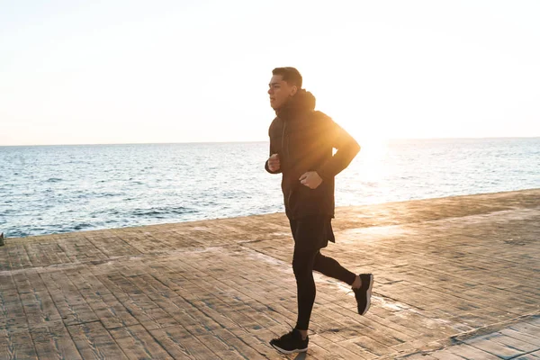 Уверенный молодой спортсмен бежит по пляжу — стоковое фото