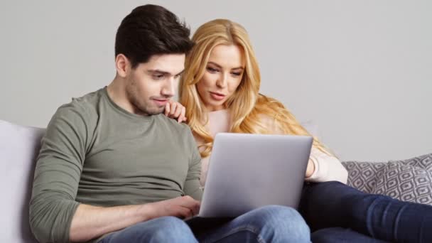 ラップトップコンピュータを使用して話しながら 自宅でソファに座って幸せなハンサムなカップル — ストック動画