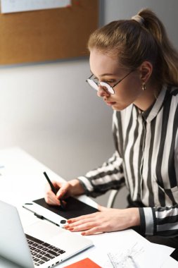 Grafik tablet bilgisayarda taslak tasarımı gözlük giyen ve işyerinde oturan sarışın Avrupalı kadın mimar Fotoğrafı