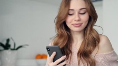 Evde mutfakta otururken çay içme ve akıllı telefon ile konuşurken Sakin gülümseyen esmer kadın 