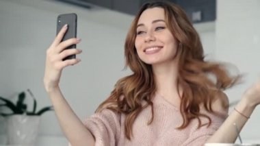 Güzel esmer kadın evde mutfakta akıllı telefon ile selfie yaparken grimacing ve gülümseyen 