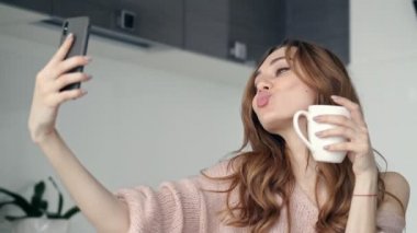 Güzel esmer kadın evde mutfakta akıllı telefon ile selfie yaparken grimacing ve gülümseyen 