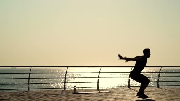 海の近くで体操をしている若いスポーツマンのシルエット — ストック動画