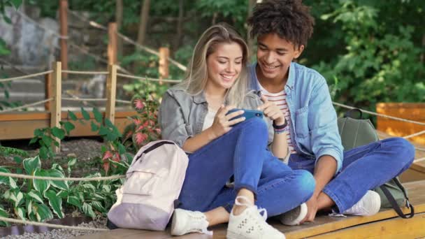 Счастливая Молодая Многонациональная Пара Пользующаяся Смартфоном Проводя Время Вместе Парке — стоковое видео
