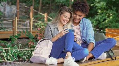 Neşeli genç çok ırklı çift akıllı telefon kullanarak ve parkta birlikte vakit geçirirken gülüyor