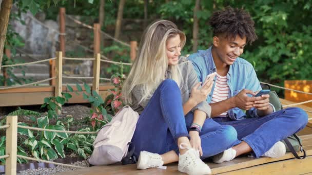 Sorrindo Jovem Casal Multiétnico Usando Smartphones Enquanto Passam Tempo Juntos — Vídeo de Stock