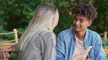 Neşeli genç çok ırklı çift akıllı telefonla müzik dinliyor ve parkta birlikte vakit geçirirken konuşuyor