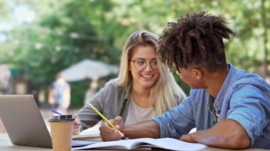 Mutlu genç çok ırklı çift şehir kafede dizüstü bilgisayar ile masanın yanında otururken bir şeyler yazma