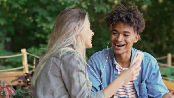 Feliz Joven Pareja Multiétnica Escuchando Música Por Teléfono Inteligente Mientras — Vídeo de stock