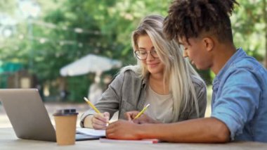 Neşeli genç çok ırklı çift şehir kafede dizüstü bilgisayar ile masanın yanında otururken bir şeyler yazma