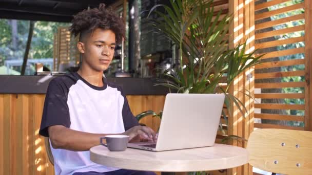 冷静的非洲学生使用笔记本电脑 而坐在户外咖啡馆的桌子旁 — 图库视频影像
