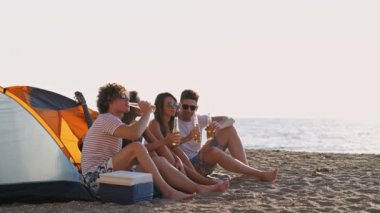 Bira içen ve deniz kenarındaki plajda birlikte eğlenen bir grup mutlu arkadaş