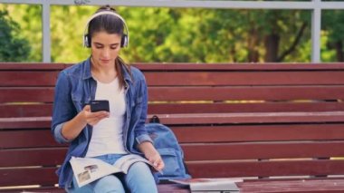 Mutlu esmer kadın akıllı telefon kullanarak ve parkta bankta otururken müzik dinleme