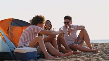Bira içen ve deniz kenarındaki plajda birlikte eğlenen bir grup genç neşeli arkadaş