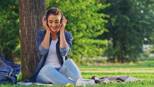 Mujer Morena Agradable Escuchando Música Por Los Auriculares Mientras Sienta — Vídeos de Stock