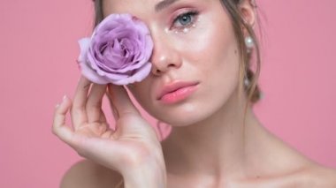 Güzel gülümseyen esmer kadının yüzünü ve ellerini pembe arka plan üzerinde çiçek le poz inci ile yakından görünümü