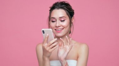 Pembe arka plan üzerinde akıllı telefon kullanarak yüz ve ellerde inci ile Güzellik mutlu dalgın esmer kadın