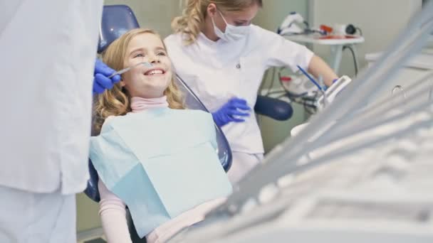 Niña Bonita Sonriendo Mientras Somete Procedimiento Dental Con Dentista Asistente — Vídeo de stock