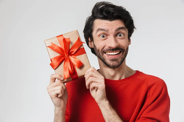 Schöner junger aufgeregter Mann posiert isoliert über weißem Wandhintergrund mit Geschenk-Box. — Stockfoto