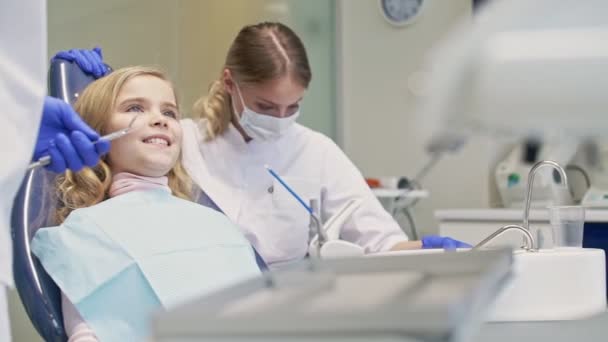 可爱的小女孩微笑 而牙科程序与牙医和助理在牙科诊所 — 图库视频影像