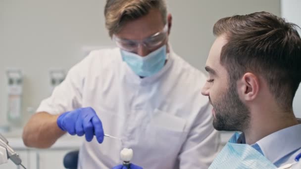 集中黑发男子听牙医他的牙齿问题 并看假牙在牙科诊所牙科手术前 — 图库视频影像