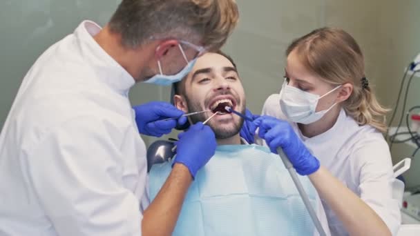 歯科医と歯科医とアシスタントとの歯科治療をしながら椅子に座っている魅力的なブルネットの男性 — ストック動画