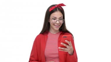 Beyaz arka plan izole üzerinde akıllı telefon kullanırken kırmızı gömlek li neşeli genç kız gülümseyerek ve kazanan jest yaparken