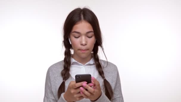 漂亮的年轻黑发女孩听无线耳机的音乐 并挥手的人 而使用智能手机在白色背景隔离 — 图库视频影像