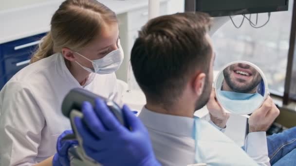 歯科医院で歯科治療後に鏡を見て微笑む おとなしいブルネットの男のバックビュー — ストック動画
