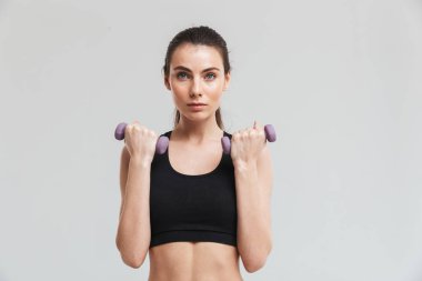 Genç spor fitness kadın gri duvar arka plan üzerinde izole dumbbells ile egzersizyapmak.